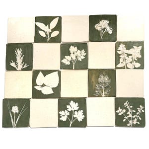 May include: A grid of square ceramic tiles, each displaying a botanical design. White plant impressions are set against a dark green backdrop. The alternating tiles are a plain off-white colour, creating a contrasting pattern.