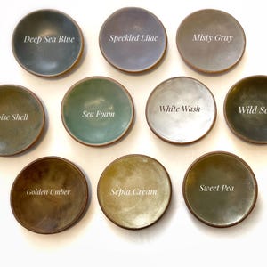 May include: Ten small ceramic dishes in various colours, including deep sea blue, speckled lilac, misty grey, white wash, sea foam, wild sage, tortoise shell, sweet pea, golden umber, and sepia cream. Each dish has a unique glaze and colour.