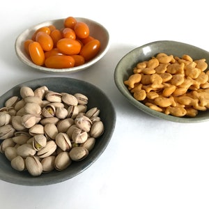 Puede incluir: Tres cuencos de cer&aacute;mica peque&ntilde;os e irregulares llenos de comida. Un cuenco contiene tomates cherry naranjas, otro contiene galletas de pez dorado y el tercero est&aacute; lleno de pistachos. Los cuencos son de tonos grises y beige.