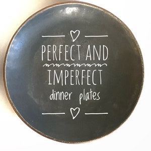 May include: A dark grey ceramic dinner plate with white lettering that reads "PERFECT AND IMPERFECT dinner plates" with a heart symbol above and below the text.