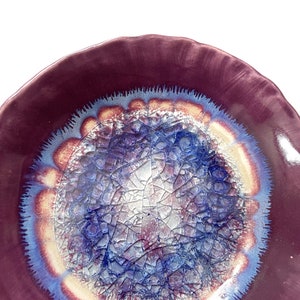 May include: A ceramic bowl with a deep purple rim and a center design of blue, white, and gold crackle glaze.