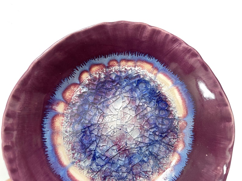 May include: A ceramic bowl with a deep purple rim and a center design of blue, white, and gold crackle glaze.