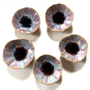 May include: Five small, ceramic bowls with a floral design. The bowls have a dark brown center, surrounded by a blend of purple, blue, and white hues. The rims are a light tan color. The bowls are arranged on a white surface.