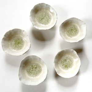 May include: Five small, circular ceramic bowls arranged in a circular pattern. Each bowl features an irregular, wavy rim with a cream-colored exterior and a textured, pale green glass center that resembles cracked or bubbled ice in appearance.