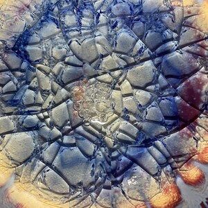 May include: Close-up of a ceramic plate with a crackled glaze in shades of blue, white, and yellow. The glaze has a textured, almost bubbly appearance.