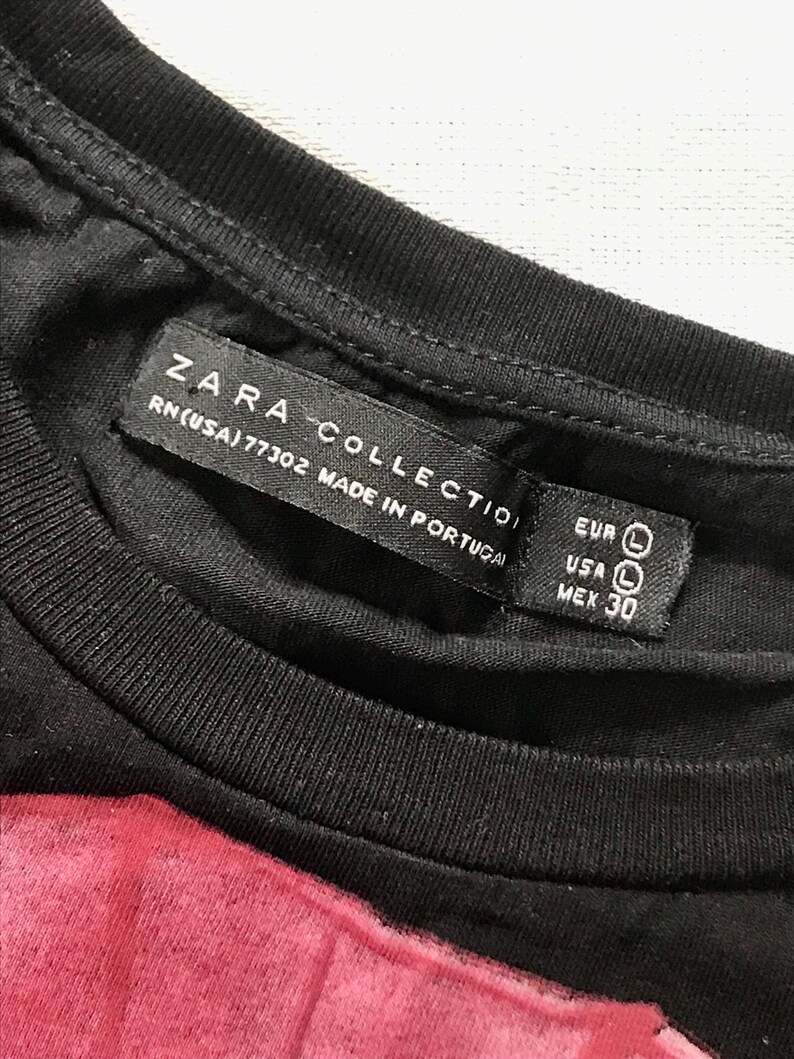 May include: Close-up of a black t-shirt with a label that reads "ZARA COLLECTION" and "RN(USA)77302 MADE IN PORTUGAL." The label also indicates size "L" for EUR and USA, and "30" for MEX.