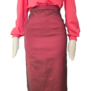 Op de afbeelding: Een rood-bordeauxkleurige potloodrok met hoge taille, gecombineerd met een koraalkleurige blouse met lange mouwen. De rok heeft een subtiele glans en een getailleerde pasvorm. De blouse heeft een klassiek knoopontwerp.