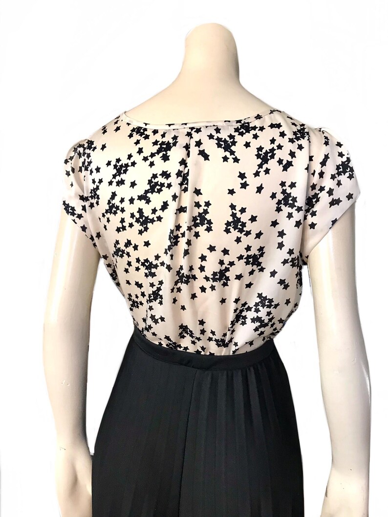 May include: A white top with a black star print and a black pleated skirt.