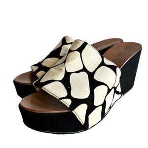 May include: A pair of platform wedge sandals. The sandals feature a black wedge heel and platform sole. The upper is cream-colored with a black organic pattern. The footbed is brown.