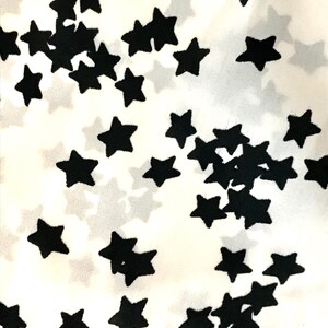 May include: White fabric with a black star pattern. The stars are scattered randomly across the fabric.