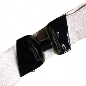 Könnte beinhalten: Ein weißes Gummiband mit einer schwarzen Plastik-Schnalle in Form einer Schleife.