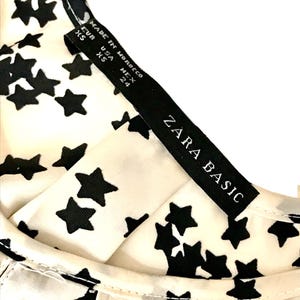 May include: A white top with a black star print and a black tag that reads "ZARA BASIC" and "MADE IN MOROCCO" with size information: EUR XS, USA XS, MEX 24.