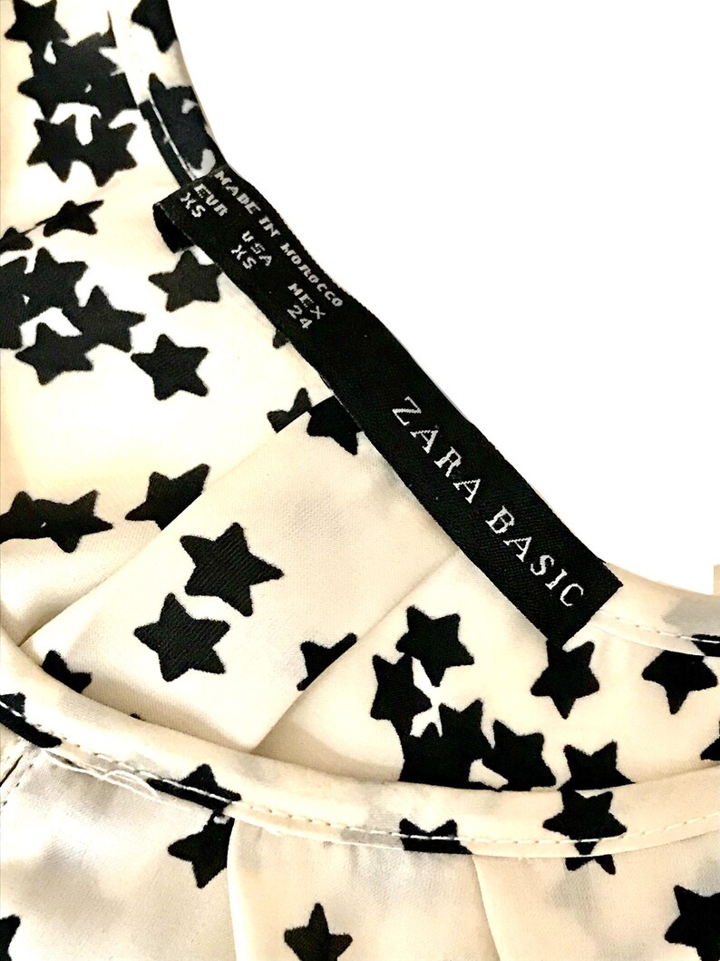 May include: A white top with a black star print and a black tag that reads "ZARA BASIC" and "MADE IN MOROCCO" with size information: EUR XS, USA XS, MEX 24.