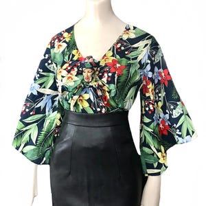 May include: A black and green floral print blouse with a knotted neckline and bell sleeves. The blouse is paired with a black leather skirt.