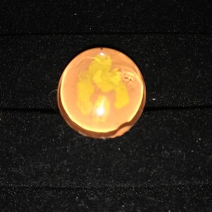 May include: A round, translucent, orange-brown glass marble with a yellow swirl design.