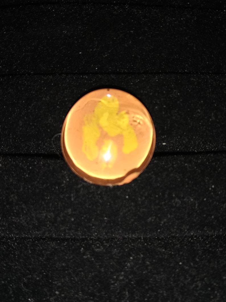 May include: A round, translucent, orange-brown glass marble with a yellow swirl design.