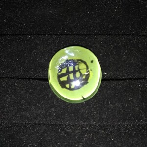 May include: A green glass marble with a black and white design inside.