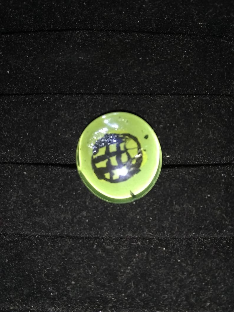 May include: A green glass marble with a black and white design inside.