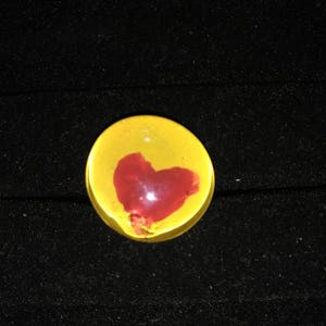 May include: A yellow glass paperweight with a red heart design.