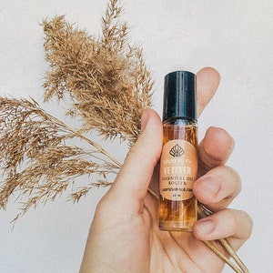 Könnte beinhalten: Eine transparente Glas-Rollflasche mit schwarzem Verschluss und einem Etikett mit der Aufschrift "VISIONS Co. VETIVER ESSENTIAL OIL ROLLER SHOPVISIONS.CO.COM 10 ML".