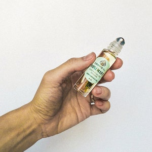May include: A clear glass roller bottle with a gold lid and a white label that says "VISIONS Co. ROSEMARY ESSENTIAL OIL  ROLL-ON  SOOTHING RELAXATION 10 ml"