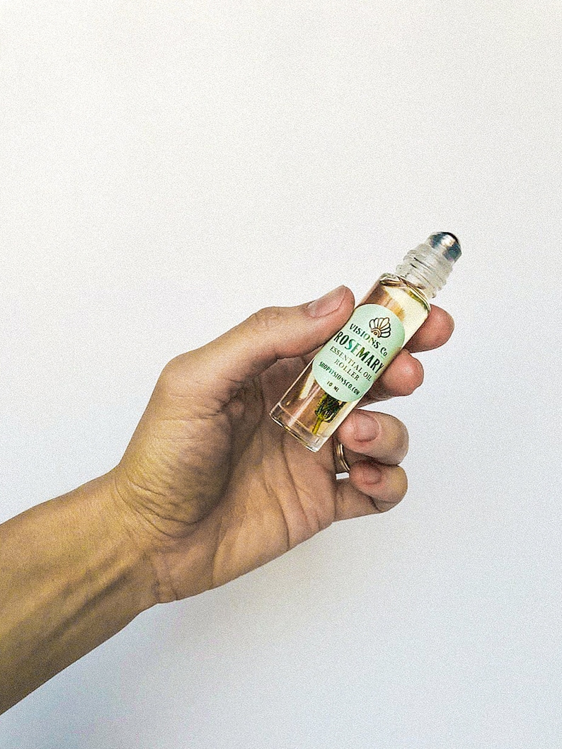 May include: A clear glass roller bottle with a gold lid and a white label that says "VISIONS Co. ROSEMARY ESSENTIAL OIL  ROLL-ON  SOOTHING RELAXATION 10 ml"