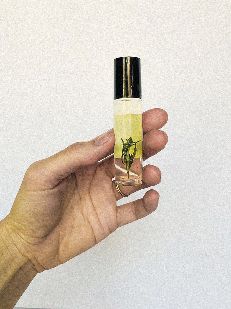 May include: A clear glass roller bottle with a black cap filled with a yellow liquid and a small green plant inside.