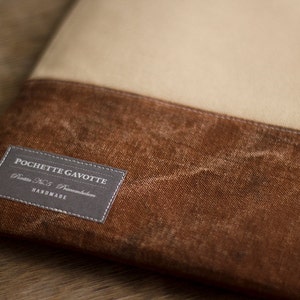 K&ouml;nnte beinhalten: Eine braune und beige Canvas-Tasche mit einem grauen Etikett, auf dem "POCHETTE GAVOTTE, Paris No. 5, Paname, HANDMADE" steht.