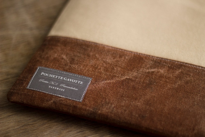K&ouml;nnte beinhalten: Eine braune und beige Canvas-Tasche mit einem grauen Etikett, auf dem "POCHETTE GAVOTTE, Paris No. 5, Paname, HANDMADE" steht.