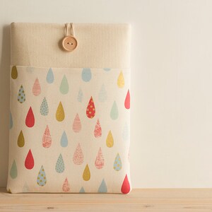 May include: A beige laptop sleeve with a flap closure and a wooden button. The sleeve is lined with a fabric featuring a repeating pattern of colorful raindrops.