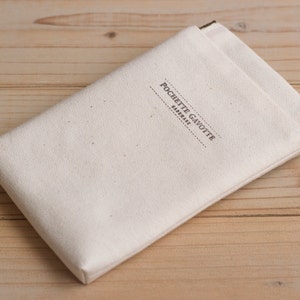 May include: Cream-coloured canvas pouch with the text "POCHETTE GAVOTTE FABRIQUE" printed in grey. The pouch has a rectangular shape with a metal clasp. The background is a light brown wooden surface.
