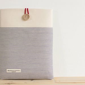 May include: A white and blue striped laptop sleeve with a red button and the text "Pochette Garotte Paris" on the front.
