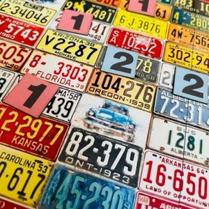 May include: A collage of vintage license plates from various states and provinces, featuring a variety of colors and designs. The plates display numbers, letters, and state names, creating a textured, eye-catching pattern. Some plates have a retro car graphic.