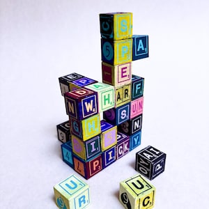 May include: A vibrant arrangement of wooden blocks, each displaying letters and numbers in a variety of colours. The blocks feature letters such as "E", "P", and "A", alongside numbers like "4" and "5". The colour palette includes blue, yellow, pink, and green.