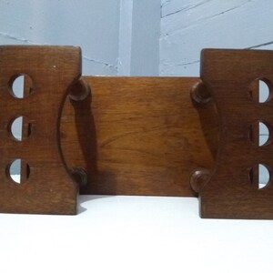 May include: A wooden bookend with a rectangular top and two curved sides. The bookend has a series of round cutouts on each side.
