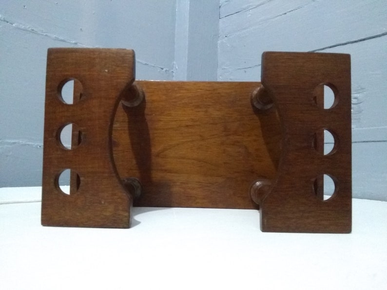 May include: A wooden bookend with a rectangular top and two curved sides. The bookend has a series of round cutouts on each side.