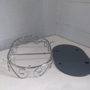 May include: A silver metal shower caddy with a decorative scroll design. The caddy is oval shaped and has a flat, gray base.