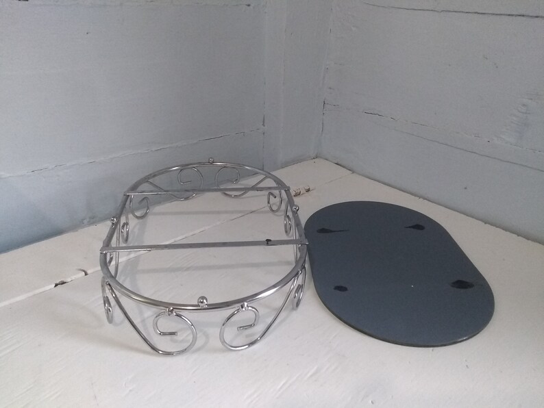 May include: A silver metal shower caddy with a decorative scroll design. The caddy is oval shaped and has a flat, gray base.