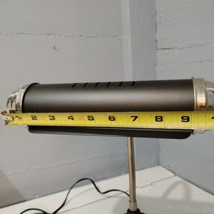 May include: A black desk lamp with a silver-colored trim. The lamp is approximately 10 inches long. It has a flexible, gooseneck-style arm and a black power cord.