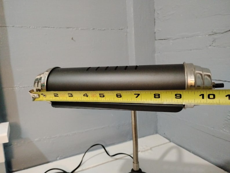 May include: A black desk lamp with a silver-colored trim. The lamp is approximately 10 inches long. It has a flexible, gooseneck-style arm and a black power cord.