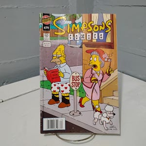 May include: A Simpsons Comics #79 comic book. The cover features cartoon characters, including an elderly man reading a book and a woman with a poodle. The comic has a yellow and blue title and a bus stop sign.