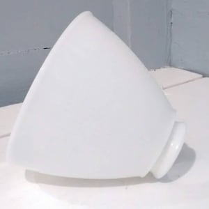 May include: A white, opaque, cone-shaped object with a rounded base. The object is smooth and appears to be made of glass or ceramic. It is resting on a white surface, with a light gray background.