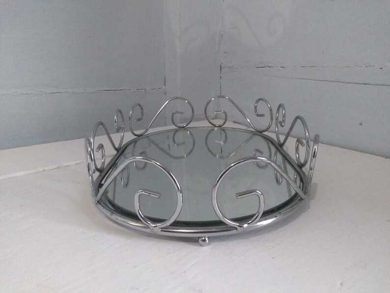 May include: A silver oval tray with a mirrored surface and a decorative scrolled border.