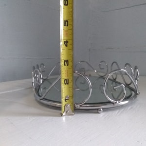 May include: A silver mirrored tray with a decorative scroll design around the edge. The tray is approximately 3 inches tall.