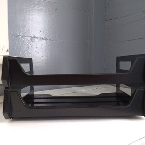 May include: Two black plastic stacking letter trays. The trays are empty and have a simple design.