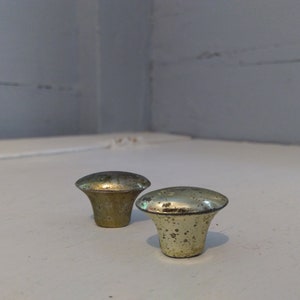 May include: Two gold-toned metal cabinet knobs with a slightly rounded top and a slightly flared base.