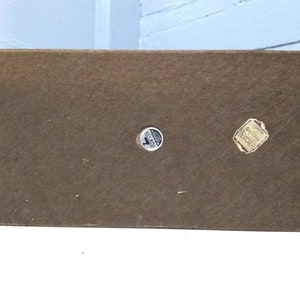 May include: The bottom of a wooden box with two round stickers. One sticker says "Genuine Walnut" and the other says "Made in USA".