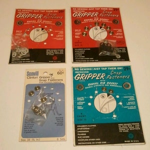 May include: Four vintage packages of Gripper snap fasteners. Two red packages and one blue package feature the text "Gripper Snap Fasteners" and "Radial Rib Socket." The fourth package is blue and white and reads "Scovill Clinton Gripper Snap Fasteners."