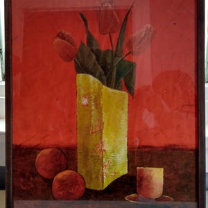 May include: A framed painting featuring a yellow vase containing red tulips, two round orange fruits, and a small cup on a dark surface against a vibrant red background. The vase displays red Chinese characters and a small red seal mark on its front side.