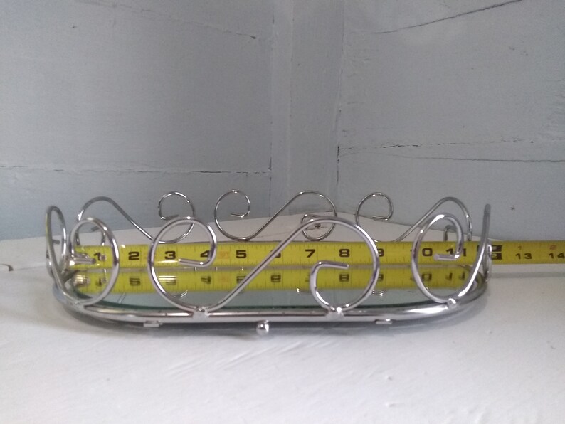 May include: A silver oval tray with a mirrored surface and a decorative scrolled metal rim. The tray is 9 inches long.